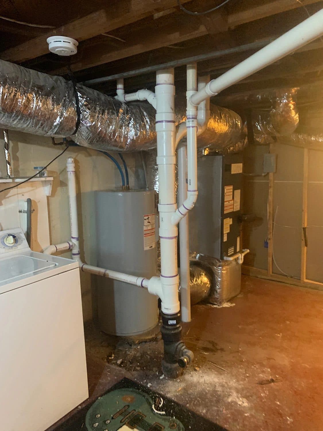 Tank water heater installed in a basement next to new PVC drain piping